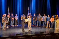 Capt. JD Crinklaw, commander, Puget Sound Naval Shipyard & Intermediate Maintenance Facility, presents Dane Bargerstock, Code 297, with an award in the Engineering or Technical (non-degreed) category, April 22, 2026, during the annual Employee of the Year ceremony at the Admiral Theatre in downtown Bremerton, Washington. (U.S. Navy photo by Jeb Fach)