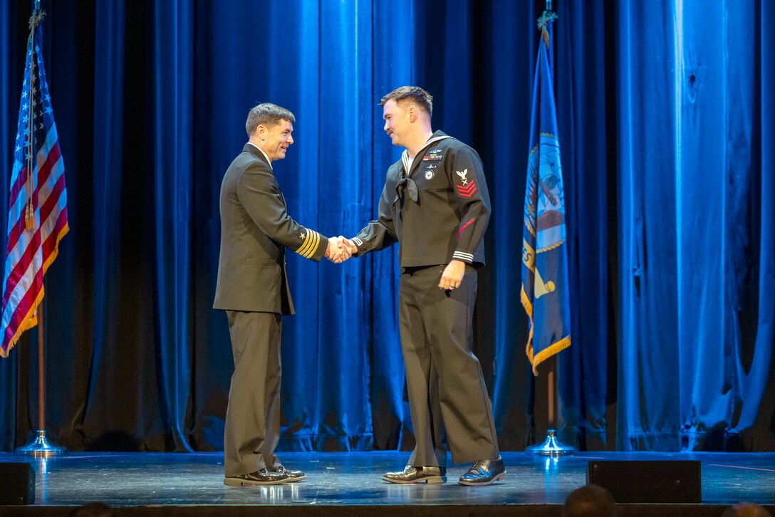 Capt. JD Crinklaw, commander, Puget Sound Naval Shipyard & Intermediate Maintenance Facility, congratulates the 2025 Sailor of the Year, Yeoman Submarine 1st Class Grant Plummer during the annual Employee of the Year ceremony at the Admiral Theatre in downtown Bremerton, Washington.. (U.S. Navy photo by Wendy Hallmark)