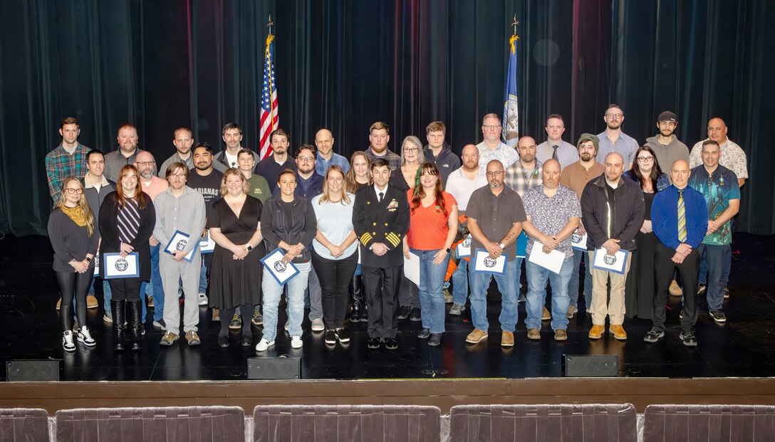 Capt. JD Crinklaw, commander, Puget Sound Naval Shipyard & Intermediate Maintenance Facility, poses for a group picture with the 2025 Employees of the Year during the annual Employee of the Year ceremony at the Admiral Theatre in downtown Bremerton, Washington. (U.S. Navy photo by Wendy Hallmark)