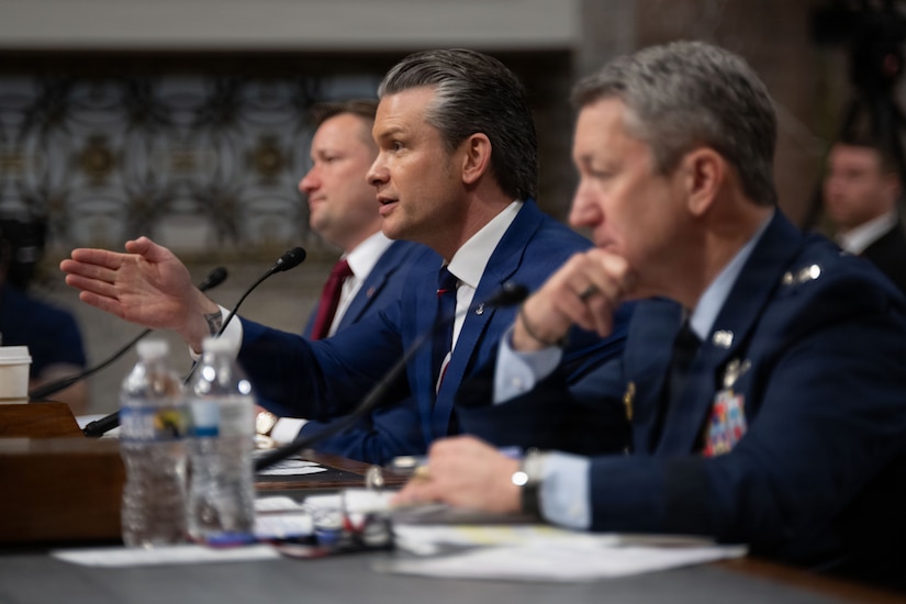 A side view of three men sitting at a table, one speaking.