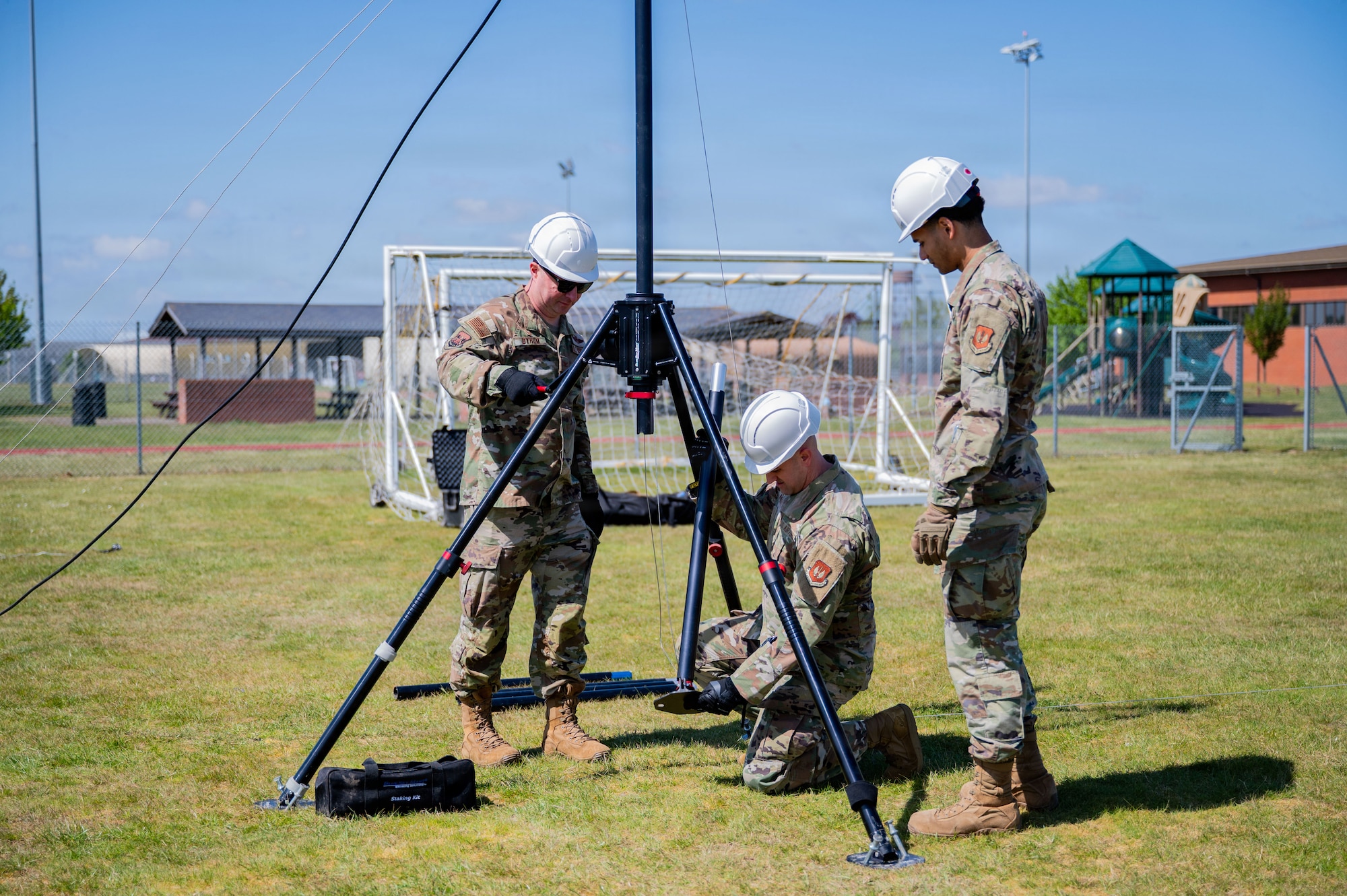 U.S. Air Force Senior Airman Savion Watson, right, 100th Communications Squadron agile combat employment technician, Chief Master Sgt. James Wall, center, 100th Air Refueling Wing command chief, and Col. Steven Byrum, 100th ARW commander, set up a horizontal dipole antenna during a day in the life integration at RAF Mildenhall, England, April 28, 2026.