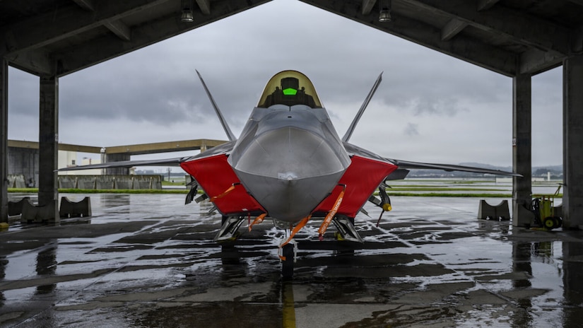 A military jet is parked under a hangar.