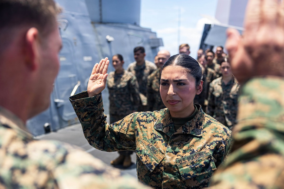 Two service members face each other while raising their right hands as fellow service members stand in formation aboard a ship on a sunny day.