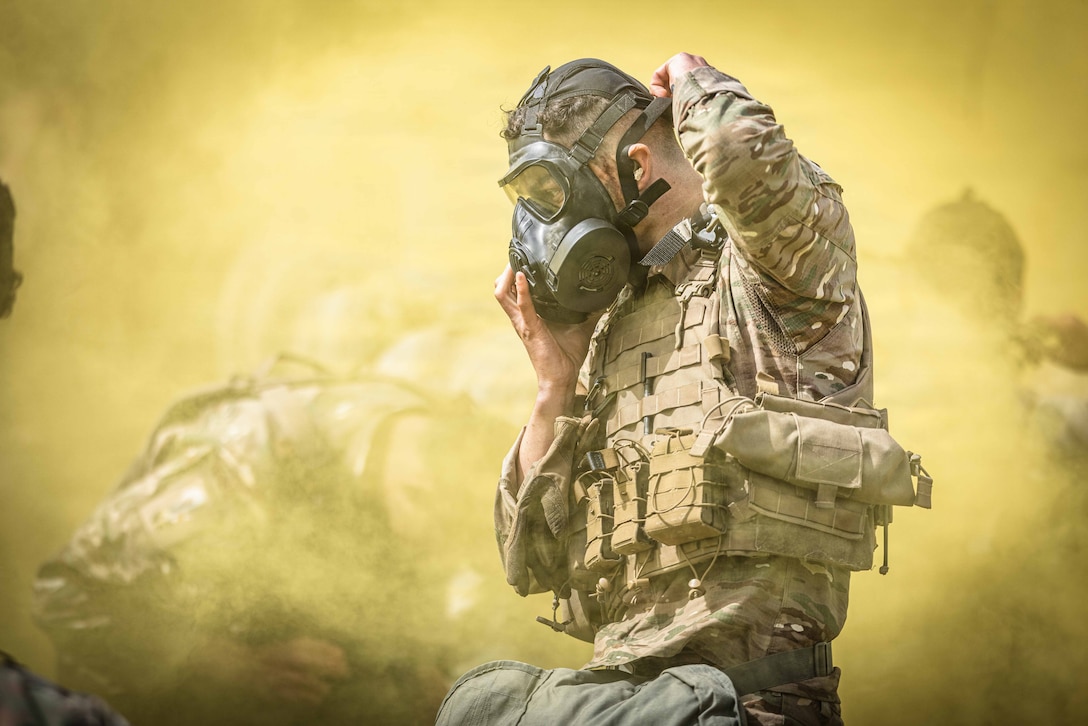 A soldier secures a gas mask, with yellow smoke in the background.