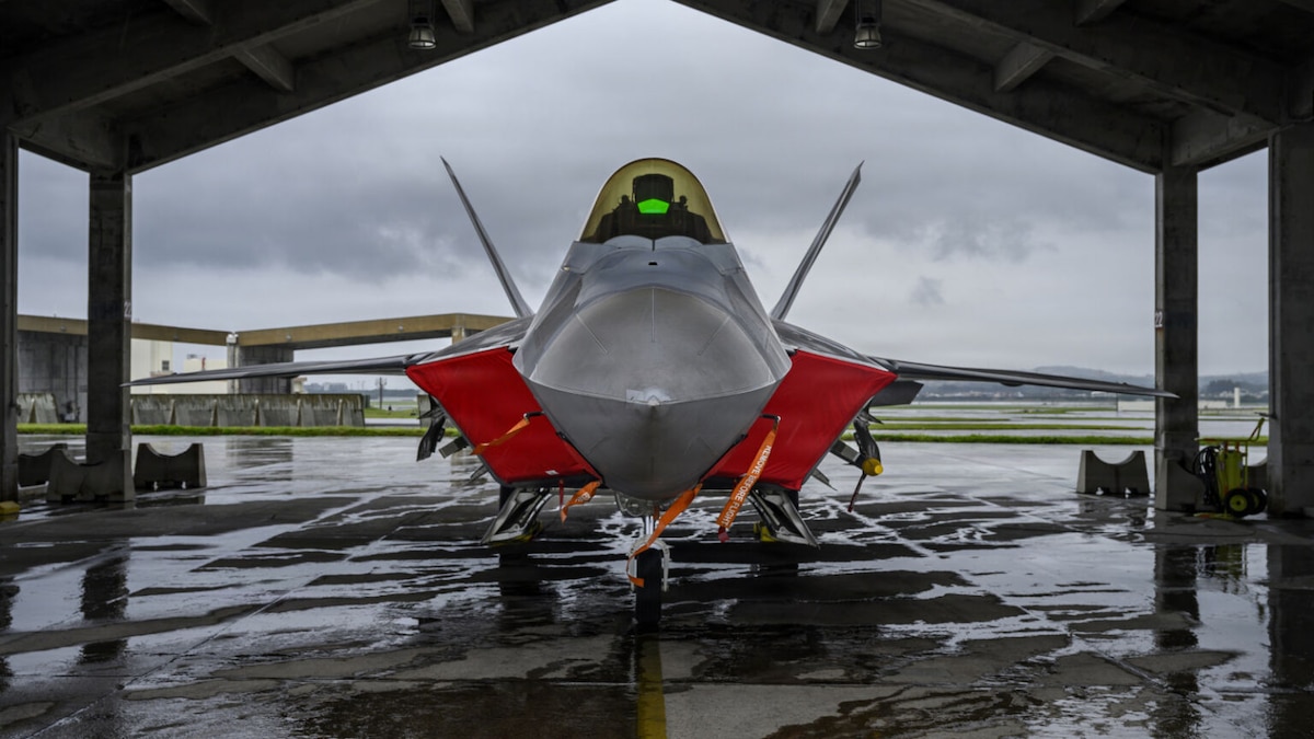 A military jet is parked under a hangar.