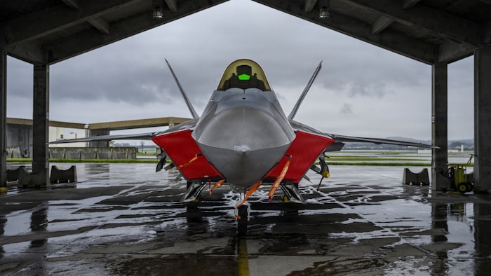 A military jet is parked under a hangar.