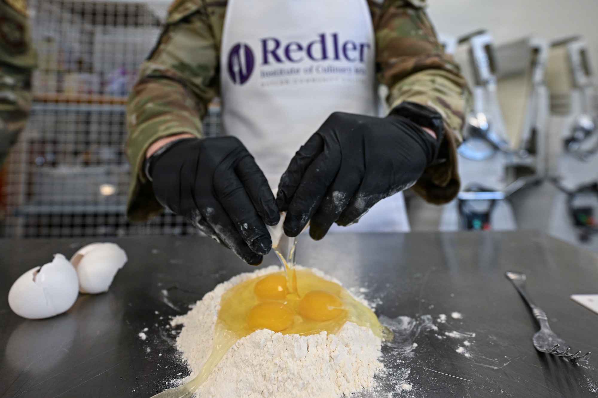 A 22nd Force Support Squadron Airman cracks an egg into a flour well at the Redler Institute of Culinary Arts in Andover, Kansas, April 28, 2026. The DFAC Airmen participated in a partnered program between Redler and McConnell Air Force Base where they had the opportunity to have expert instruction on two separate recipes. (U.S. Air Force photo by Senior Airman Amelio Brown)
