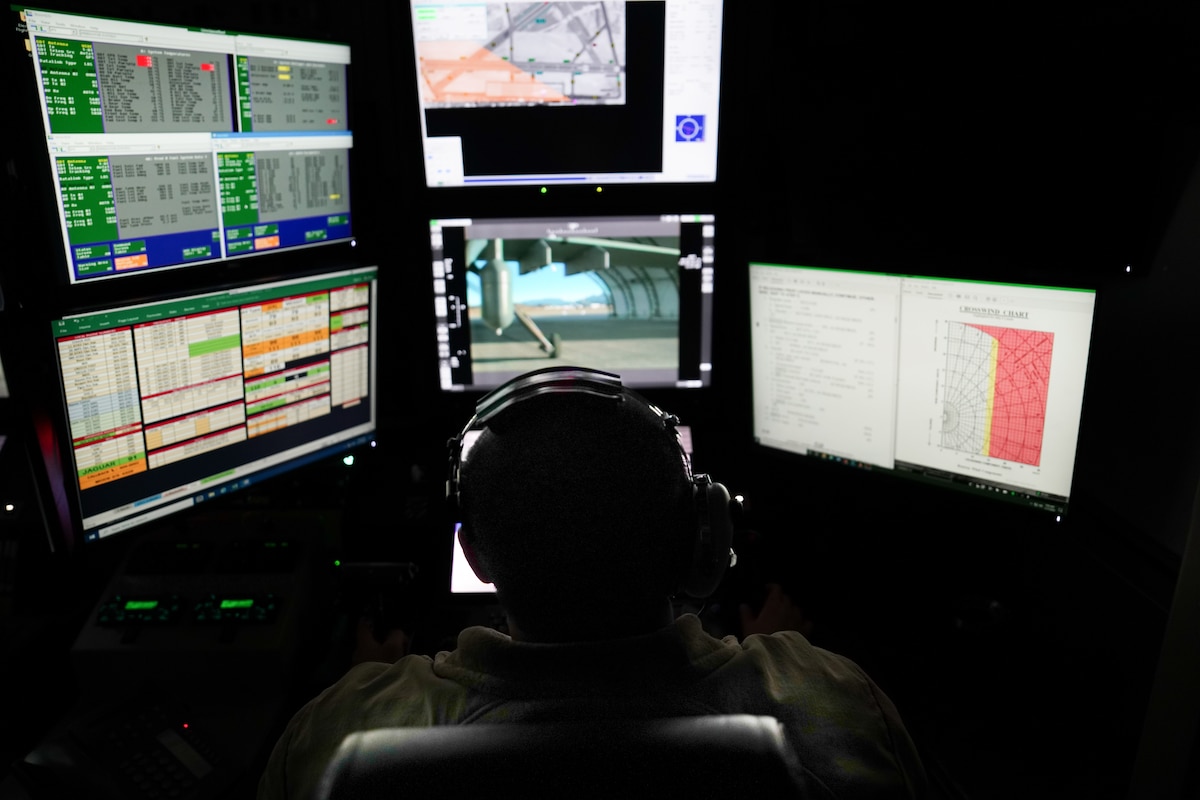 A man operates controls and watches multiple screens in a remotely piloted aircraft ground control station.