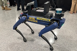 A robotic dog bears the words "MAVERICK CHASER" on the side. Mounted to its top is an array of electronic equipment.