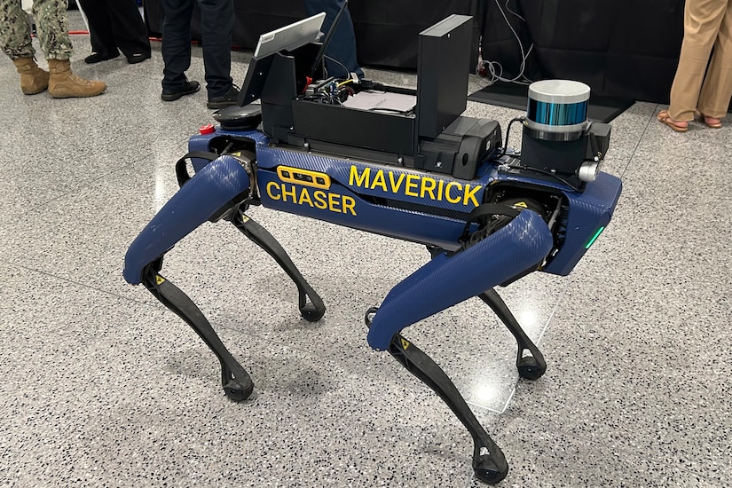 A robotic dog bears the words "MAVERICK CHASER" on the side. Mounted to its top is an array of electronic equipment.
