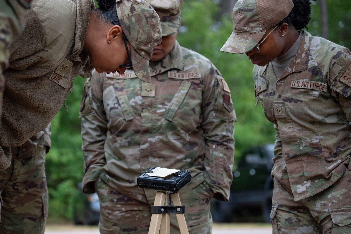 Three Airmen look a piece of paper on a stand