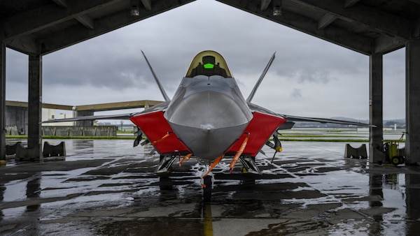 A military jet is parked under a hangar.