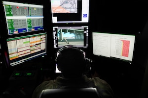 A man operates controls and watches multiple screens in a remotely piloted aircraft ground control station.