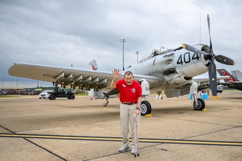 An Eagle waving while standing in front of a prop airplane