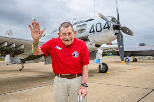 An Eagle waving, while standing in front of a prop airplane