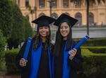Two women smile while wearing graduation caps and gowns.