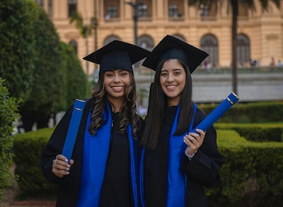 Two women smile while wearing graduation caps and gowns.