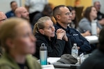 People sit and listen in a large room.