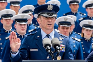 A man in uniform raises his right hand to admister the Oath of Office to U.S. Air Force Academy graduates.