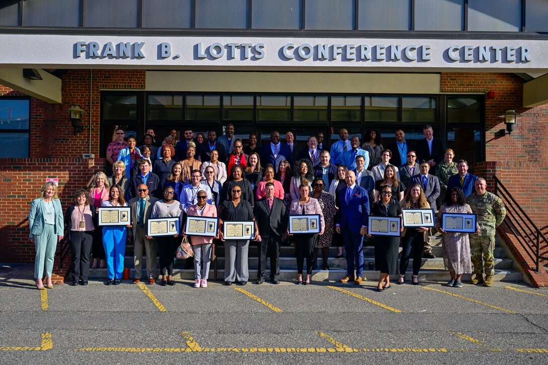 A large group of employees stand on stairs in front of a building holding their certificates.
