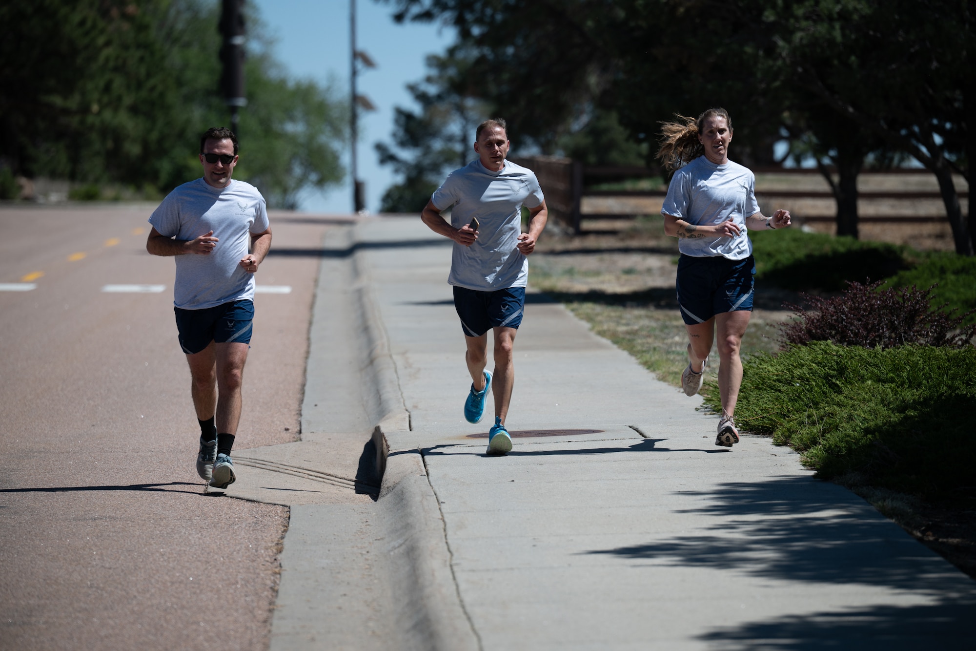 Three Airmen jog down a road together.