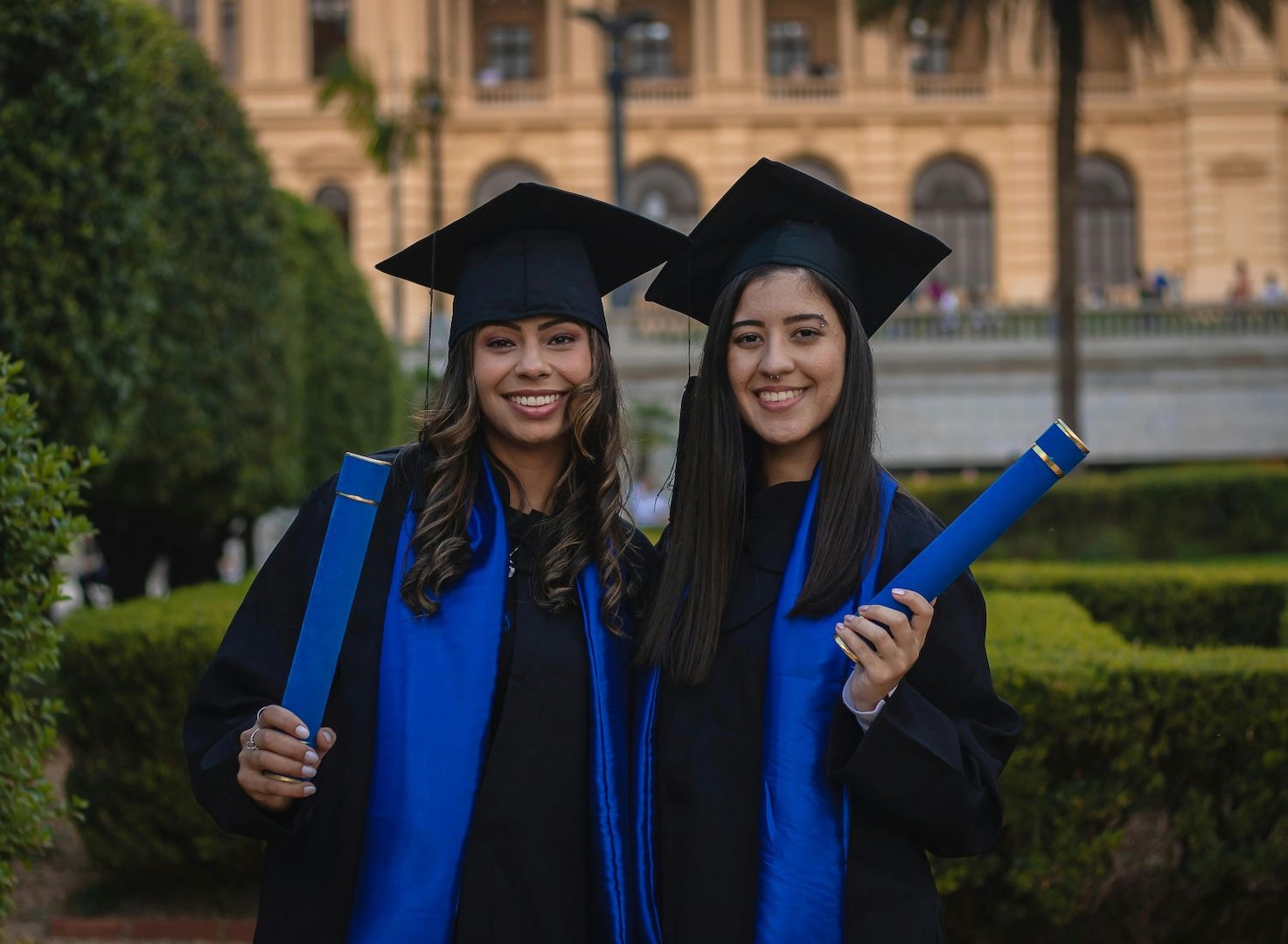 Two women smile while wearing graduation caps and gowns.