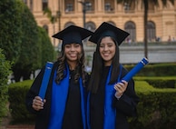 Two women smile while wearing graduation caps and gowns.