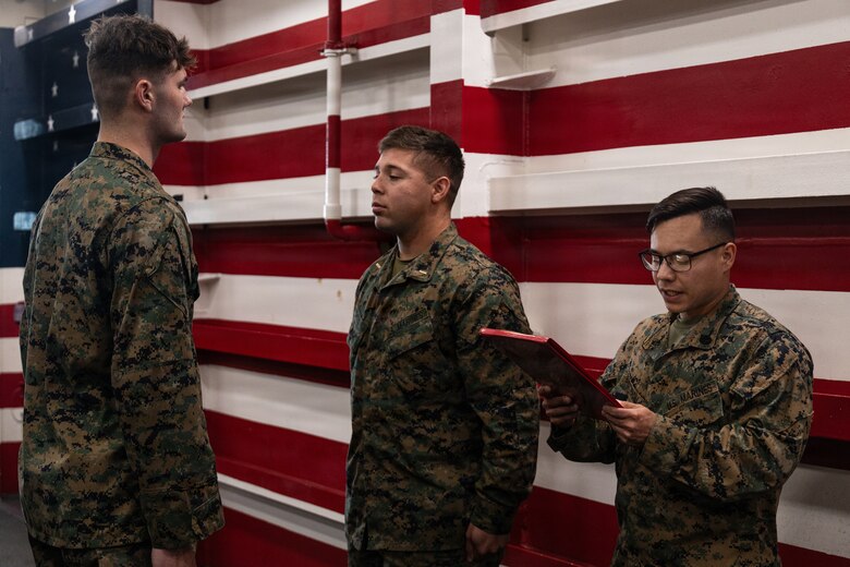 U.S. Marine Corps Staff Sgt. Christopher Baez Padilla, right, a platoon sergeant with Lima Company, Battalion Landing Team 3/5, 11th Marine Expeditionary Unit, reads a promotion warrant in the well deck of San Antonio-class amphibious transport dock ship USS Portland (LPD 27), during a promotion ceremony in the Pacific Ocean, Dec. 7, 2025. The 11th MEU is currently underway aboard the Boxer Amphibious Ready Group in the U.S. 3rd Fleet area of operations conducting integrated training that enhances lethality and warfighting readiness. (U.S. Marine Corps photo by Lance Cpl. Luke Rodriguez)