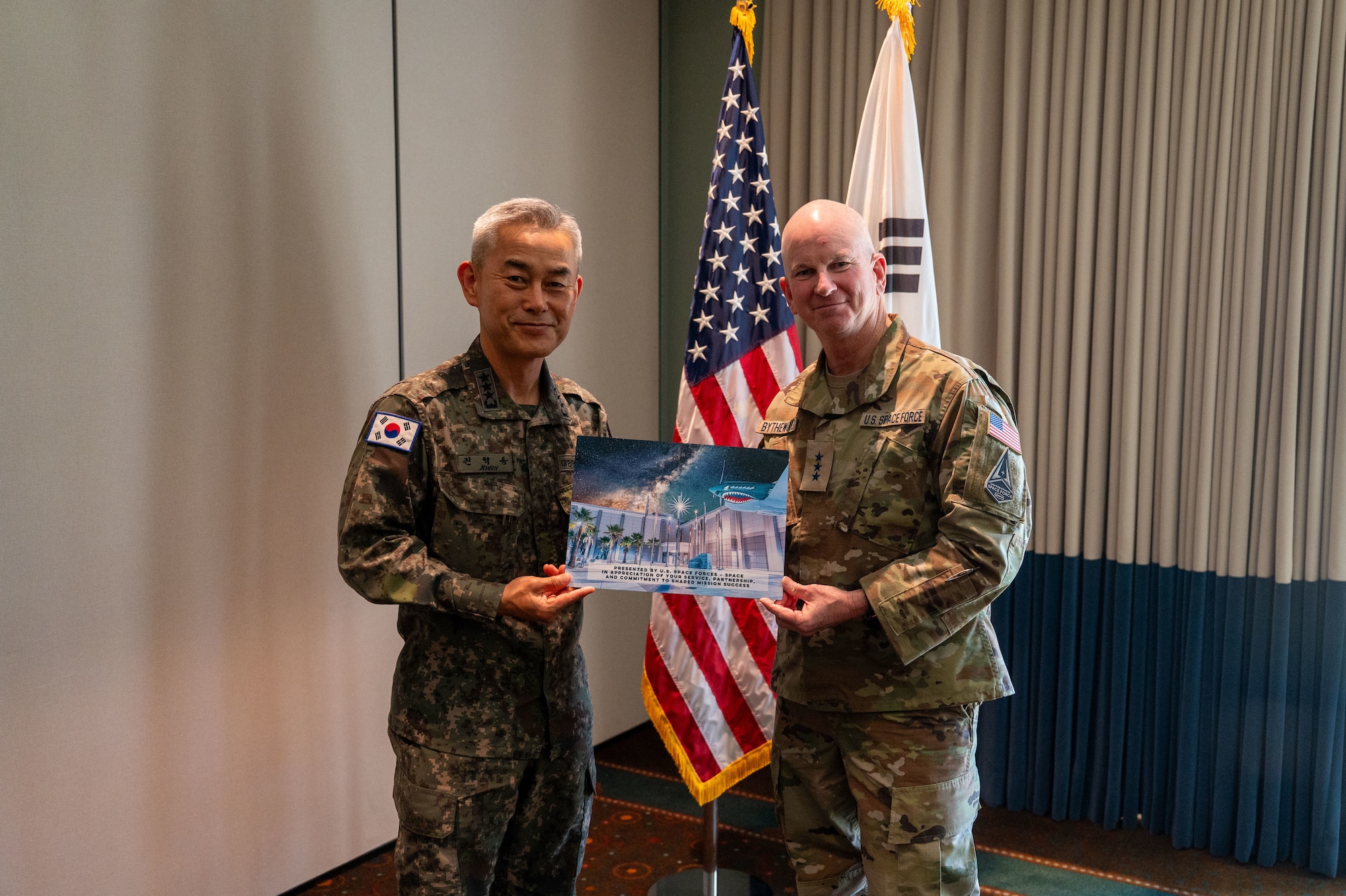 An American and Korean man hold up a plaque with a stylized photo of the S4S headquarters building with the stars out at night