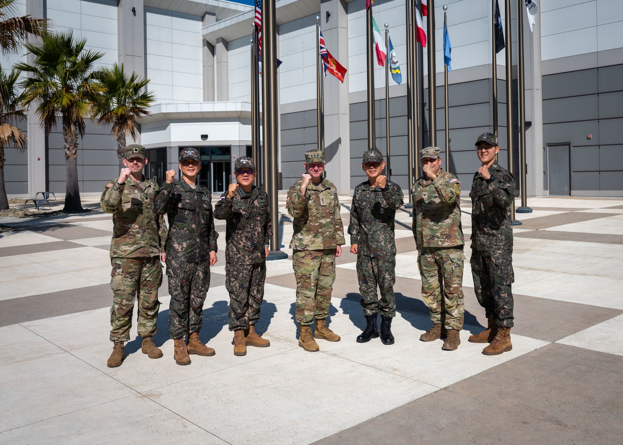 Seven intermingled military uniformed men clench their fists in solidarity in front of flags from around the world