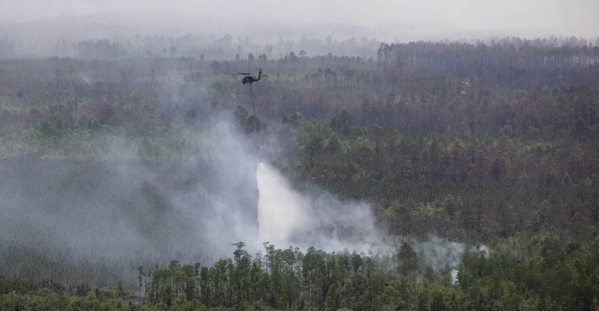 A UH-60 Blackhawk helicopter crew with Charlie Company, 1st General Support Aviation Battalion, 106th Aviation Regiment, 78th Aviation Troop Command, Georgia Army National Guard, drops water from its Bambi Bucket on an active fire during the wildfire suppression efforts in Pineland, Georgia, April 25, 2026. The Georgia Department of Defense plays an integral role in declared emergencies by providing a versatile and ready force capable of responding to natural and manmade disasters across the United States. (U.S. Army National Guard photo by Sgt. Jordan McNeal)