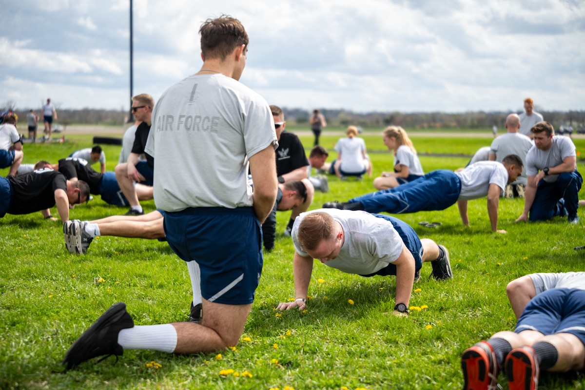 A large group, wearing Air Force fitness attire, do push-ups in the grass
