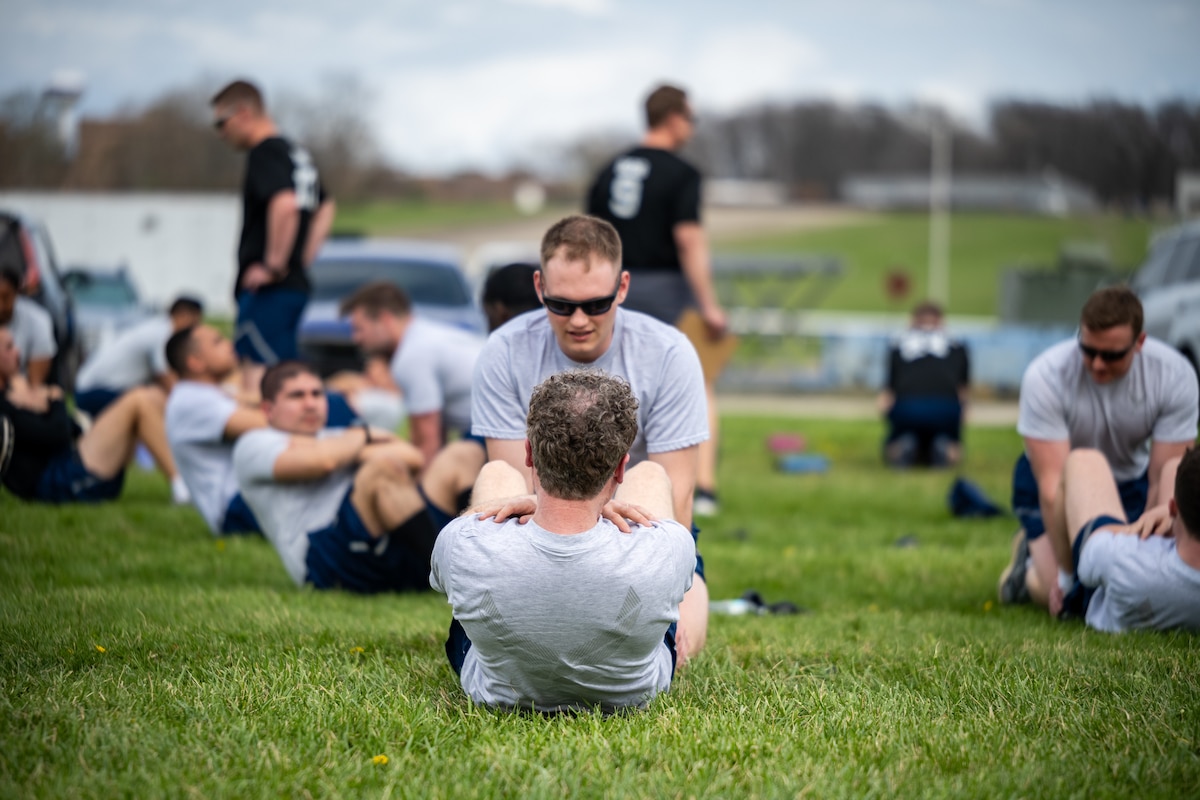 Members in Air Force physical fitness attire complete sit-ups in the grass