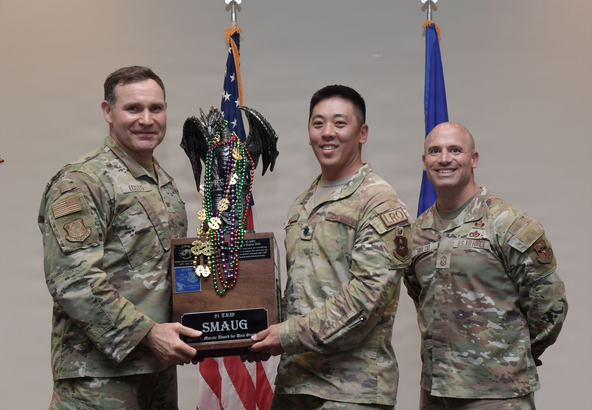 Three men in military uniform hold a trophy.