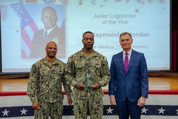260504-N-KC192-1026 PORTSMOUTH, Va. (May 4, 2026) Lt. Raymond Jordan, center., assigned to Naval Medical Forces Atlantic, is presented the Junior Logistician of the Year Award by Dr. Michael McGinnis, Bureau of Medicine and Surgery (BUMED) executive director, during the 2026 Medical Logistics Symposium held on board Naval Medical Center Portsmouth, May 4, 2026. Jordan was recognized for improving logistics processes and managing deployment-ready medical materiel, strengthening the speed, accountability and effectiveness of expeditionary medical support. The Navy Medicine Logistics Symposium aims to maintain a common operating picture and update the Medical Logistics community reagarding the fiscal year 2026 Navy Medicine Campaign Order and the Navy MEDLOG goal to build a logistics system that delivers ready operational units to support the Naval Strategy. (U.S. Navy photo by Mass Communication Specialist Second Class Levi Decker)