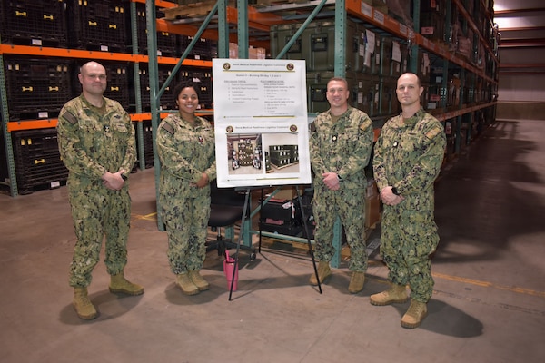 260504-N-VL857-1002 WILLIAMSBURG, Va. (May 5, 2026) Sailors assigned to Naval Medical Readiness Logistics Command (NMRLC) pose with a display showcasing statistics of Station 5 on board NMRLC – Cheatham Annex, Williamsburg, Va., May 5, 2026. Sailors hosted facility tours during the 2026 Navy Medicine Logistics Symposium that spanned much of the Hampton Roads and Tidewater, Va. area. During the tour, Sailors briefed  visitors on the Expeditionary Resuscitative Surgical Suite (ERSS) and the En Route Care System (ERCS). (U.S. Navy photo by Julius Evans)