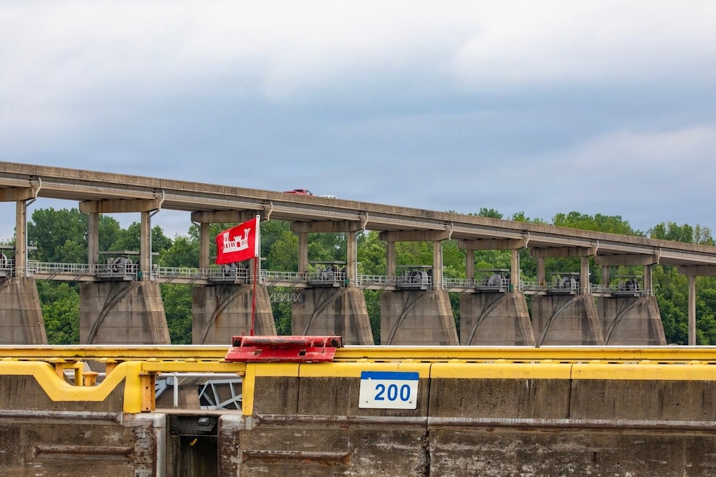 a car driving on a road over a dam with woods in the background.
