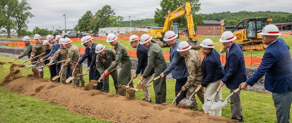 several people in white hard hats using shovels on a long pile of earth