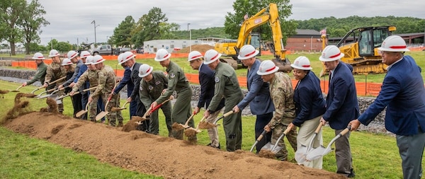 several people in white hard hats using shovels on a long pile of earth