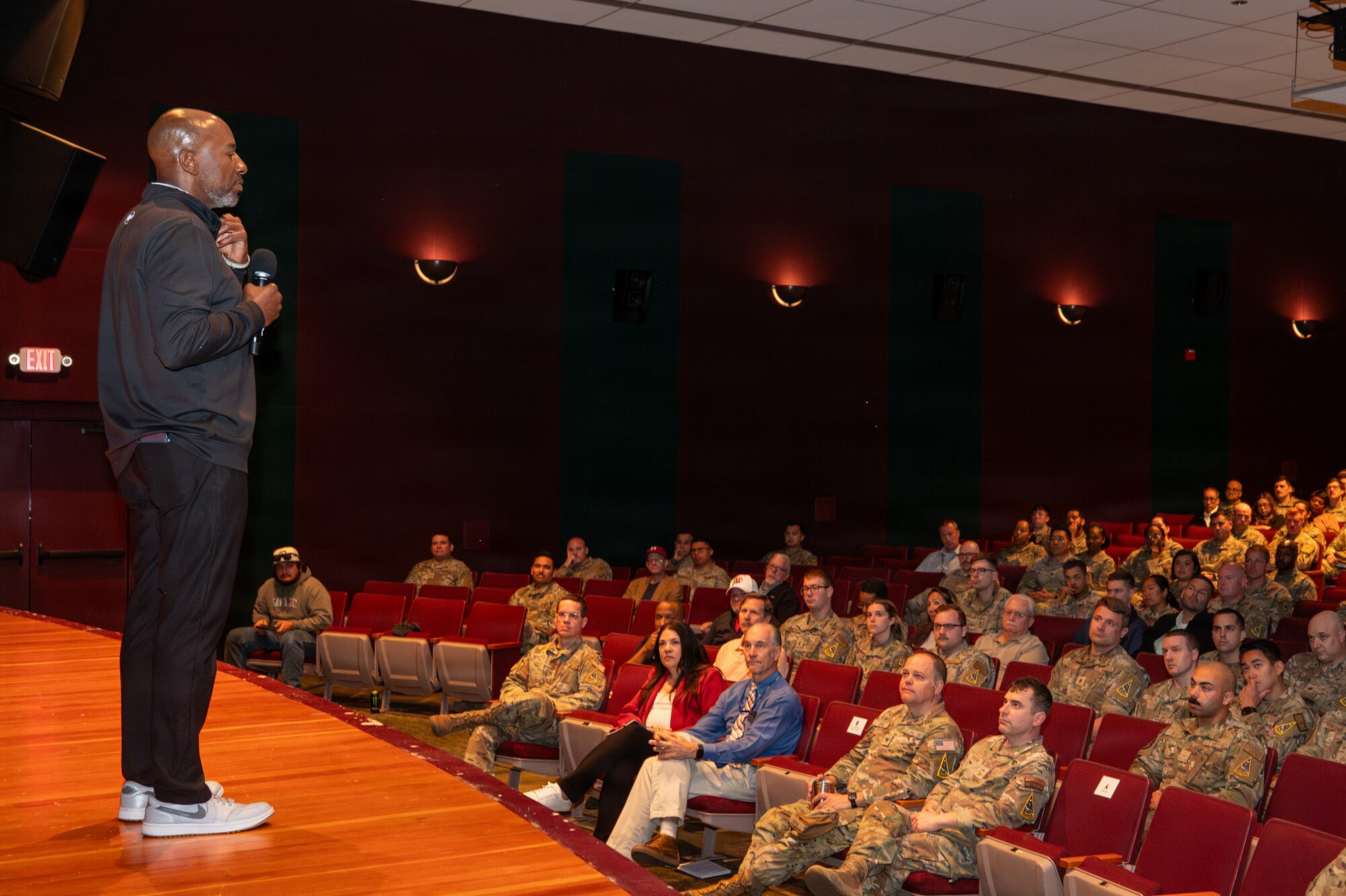 Kaleth O. Wright stands on a stage and looks out into an audience of people sitting in theater chairs.