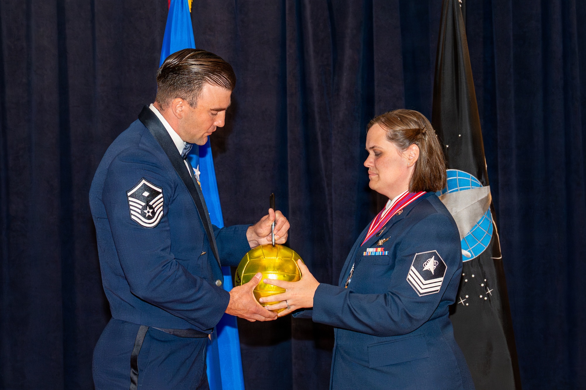 U.S. Air Force Master Sgt. Brian Johnson signs a volleyball held between him and another servicemember.
