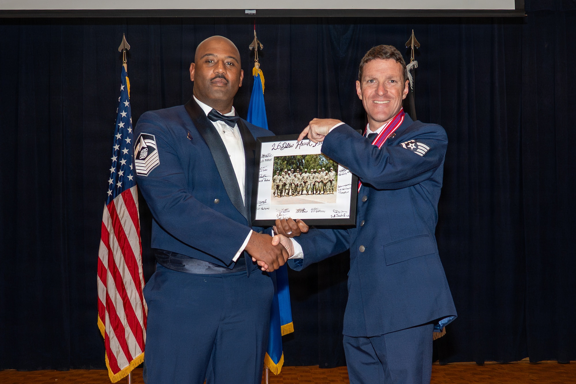 Two people stand on stage for an award photo. They are holding a framed picture.