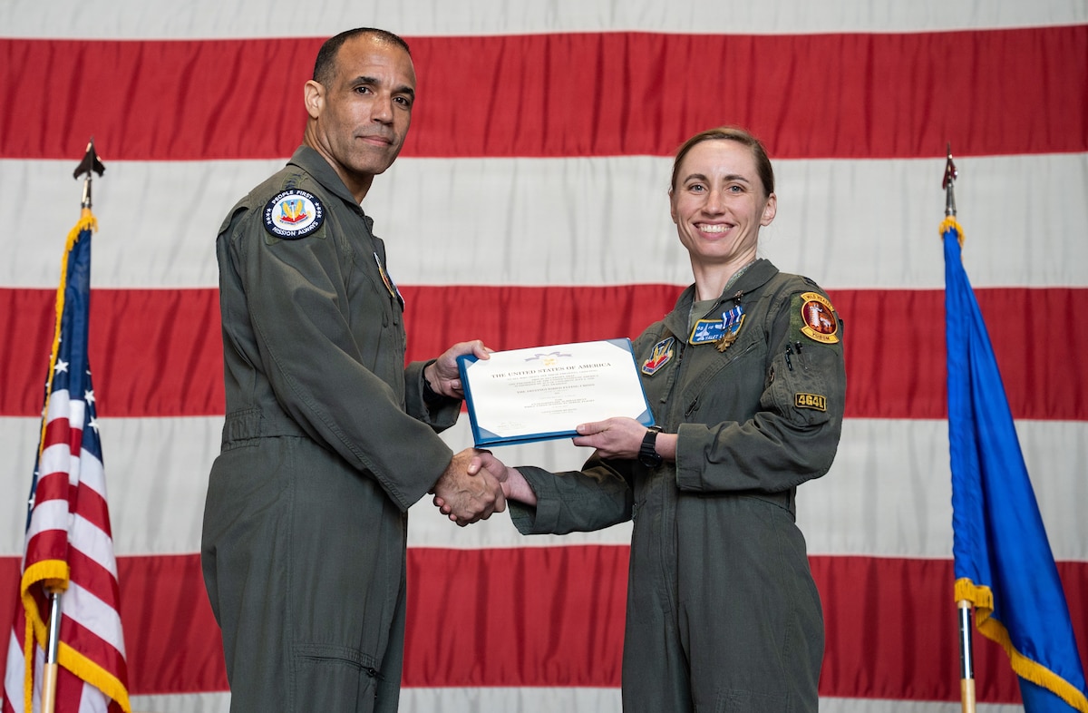 Two Air Force pilots hold a certificate with a giant American flag in the background