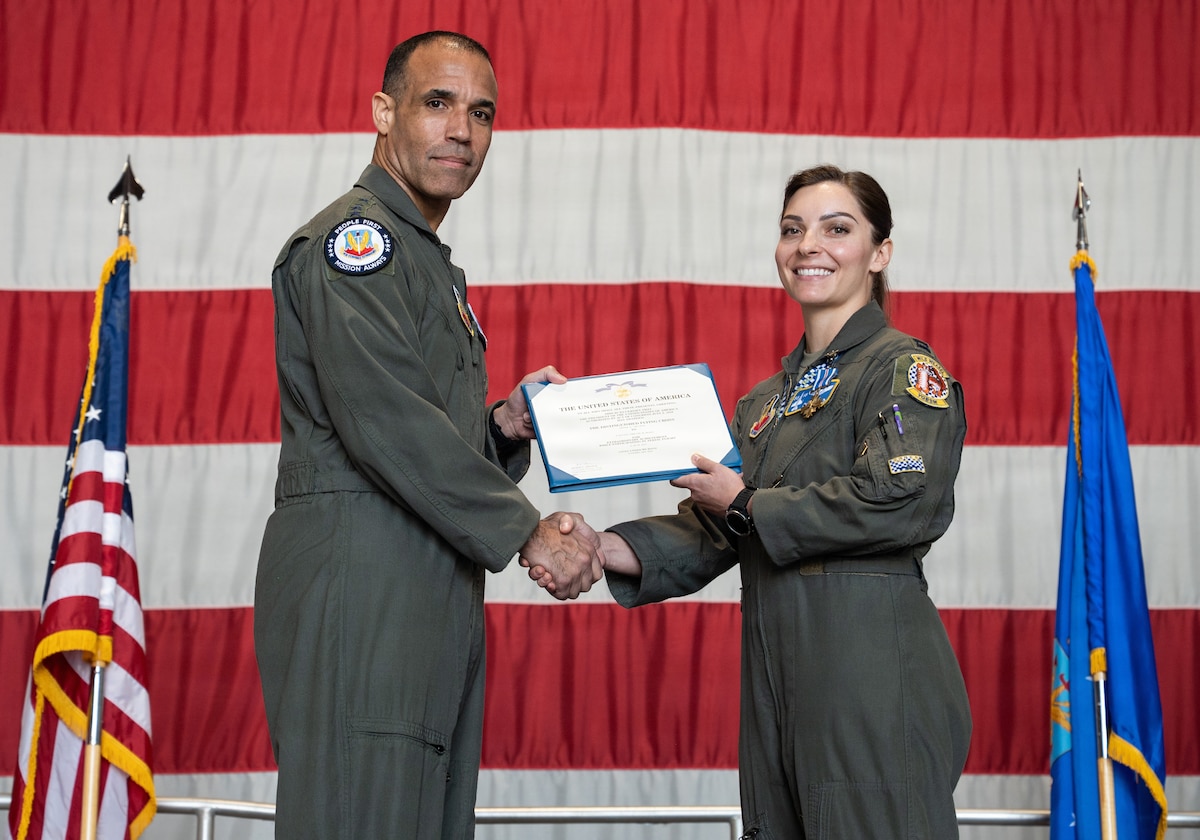 Two Air Force pilots hold a certificate with a giant American flag in the background