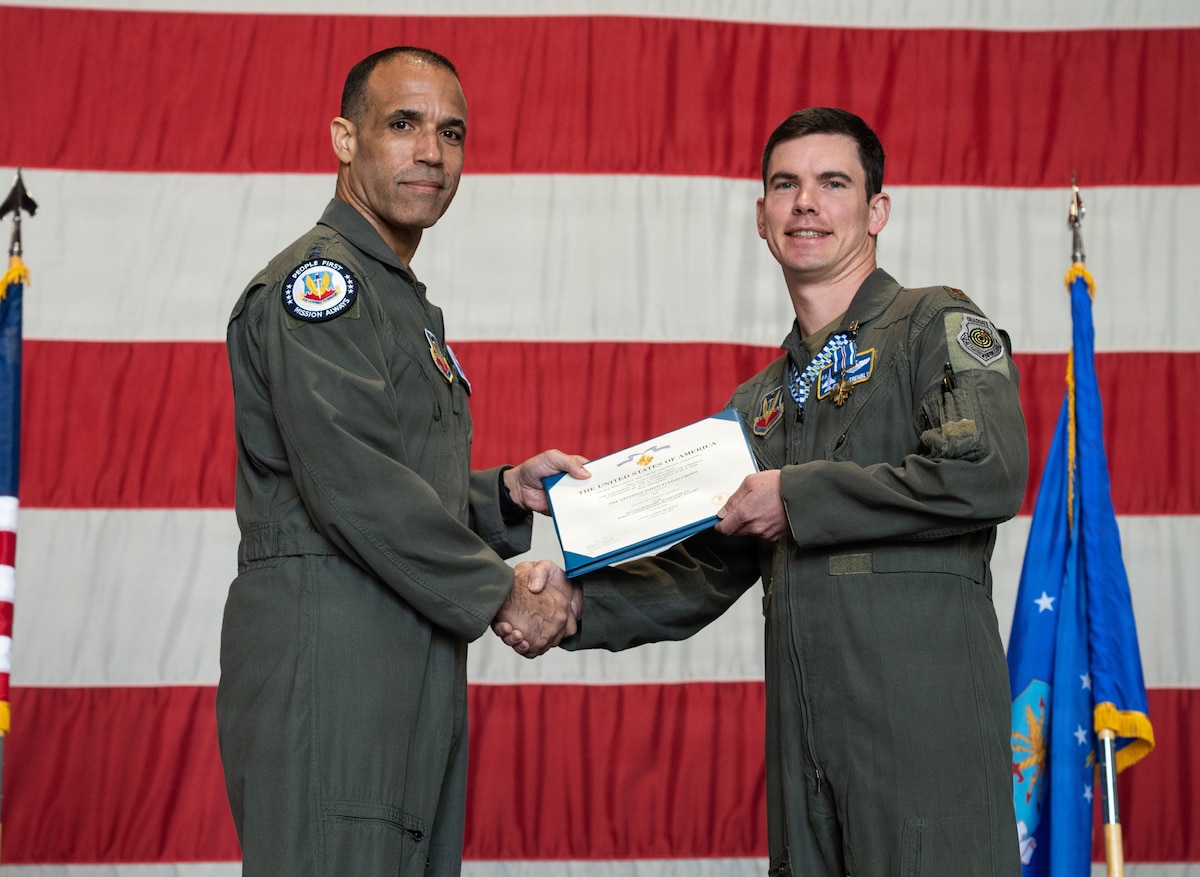 Two Air Force pilots hold a certificate with a giant American flag in the background