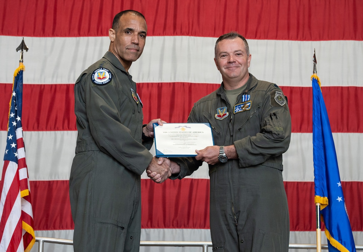 Two Air Force pilots hold a certificate with a giant American flag in the background