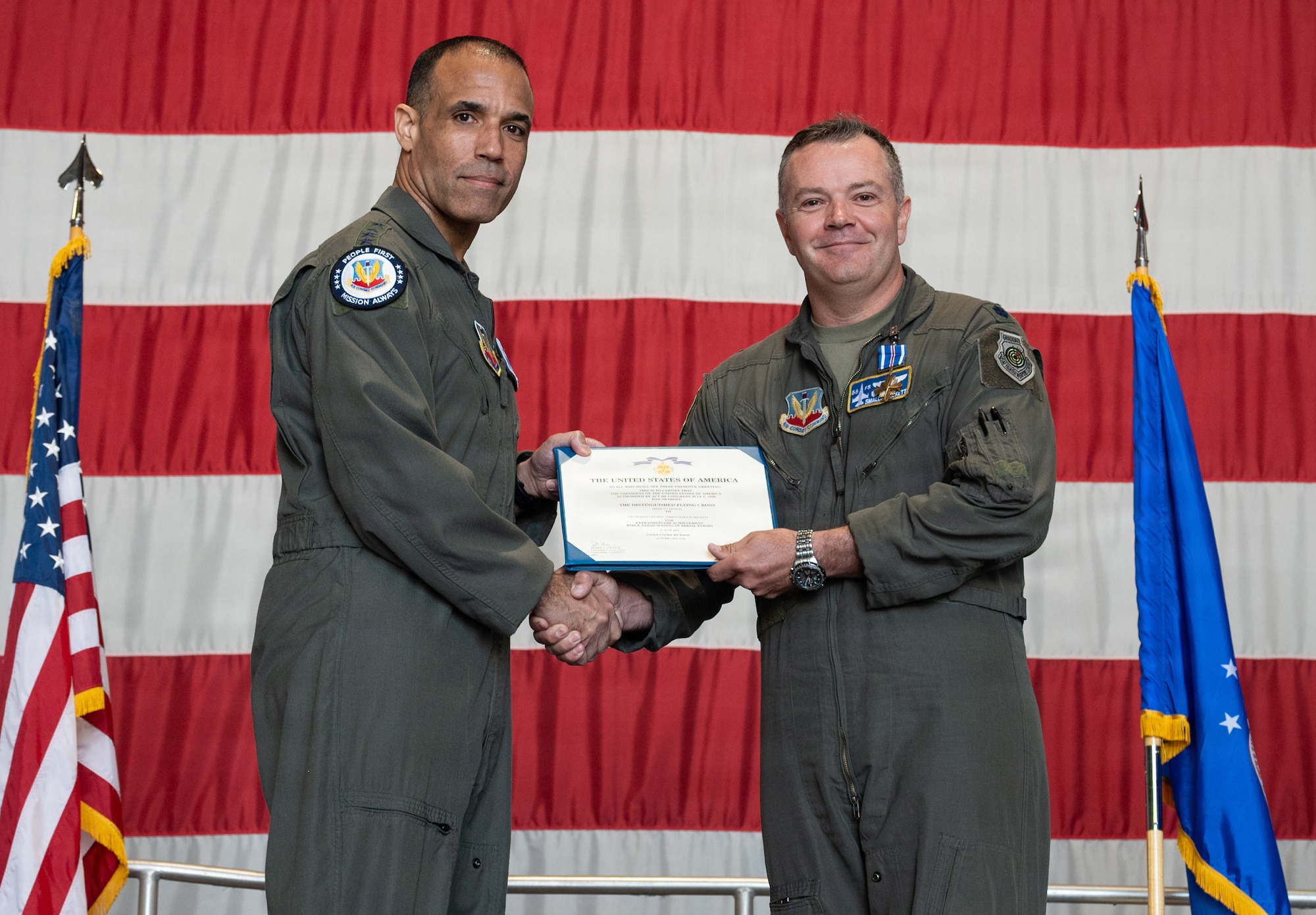 Two Air Force pilots hold a certificate with a giant American flag in the background