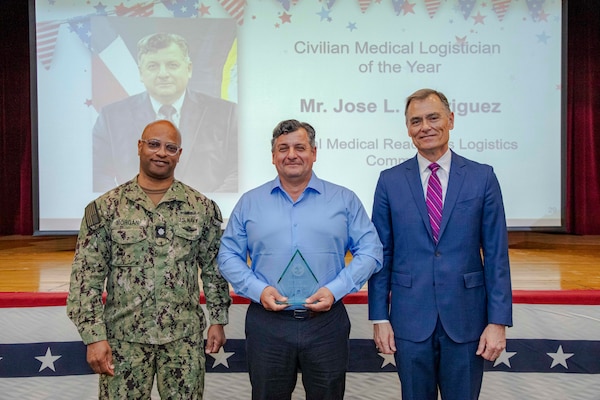 260504-N-KC192-1049 PORTSMOUTH, Va. (May 4, 2026) Jose Rodriguez, center, with Navy Medicine Readiness and Logistics Command, is presented the Civilian Medical Logistician of the Year Award by Dr. Michael McGinnis, Bureau of Medicine and Surgery (BUMED) executive director, during the 2026 Medical Logistics Symposium held on board Naval Medical Center Portsmouth, May 4, 2026. Rodriguez was recognized for synchronizing global medical logistics and sustainment efforts, enabling rapid distribution of materiel critical to expeditionary medical missions worldwide. The Navy Medicine Logistics Symposium aims to maintain a common operating picture and update the Medical Logistics community regarding the fiscal year 2026 Navy Medicine Campaign Order and the Navy MEDLOG goal to build a logistics system that delivers ready operational units to support the Naval Strategy. (U.S. Navy photo by Mass Communication Specialist Second Class Levi Decker)