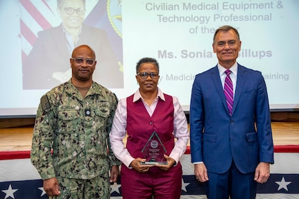 260504-N-KC192-1052 PORTSMOUTH, Va. (May 4, 2026)  Sonia Billups, with Navy Medicine Operational Training Command, is presented the Civilian Medical Equipment and Technology Professional of the Year Award by Dr. Michael McGinnis, Bureau of Medicine and Surgery (BUMED) executive director, during the 2026 Medical Logistics Symposium held on board Naval Medical Center Portsmouth, May 4, 2026. Billups was recognized for advancing property management and technical support systems, strengthening the accountability and readiness of equipment used in expeditionary operations. The Navy Medicine Logistics Symposium aims to maintain a common operating picture and update the Medical Logistics community regarding the fiscal year 2026 Navy Medicine Campaign Order and the Navy MEDLOG goal to build a logistics system that delivers ready operational units to support the Naval Strategy. (U.S. Navy photo by Mass Communication Specialist Second Class Levi Decker)