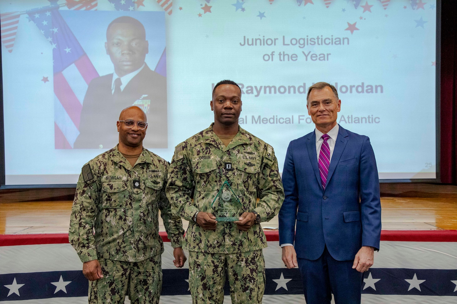 260504-N-KC192-1026 PORTSMOUTH, Va. (May 4, 2026) Lt. Raymond Jordan, center., assigned to Naval Medical Forces Atlantic, is presented the Junior Logistician of the Year Award by Dr. Michael McGinnis, Bureau of Medicine and Surgery (BUMED) executive director, during the 2026 Medical Logistics Symposium held on board Naval Medical Center Portsmouth, May 4, 2026. Jordan was recognized for improving logistics processes and managing deployment-ready medical materiel, strengthening the speed, accountability and effectiveness of expeditionary medical support. The Navy Medicine Logistics Symposium aims to maintain a common operating picture and update the Medical Logistics community reagarding the fiscal year 2026 Navy Medicine Campaign Order and the Navy MEDLOG goal to build a logistics system that delivers ready operational units to support the Naval Strategy. (U.S. Navy photo by Mass Communication Specialist Second Class Levi Decker)